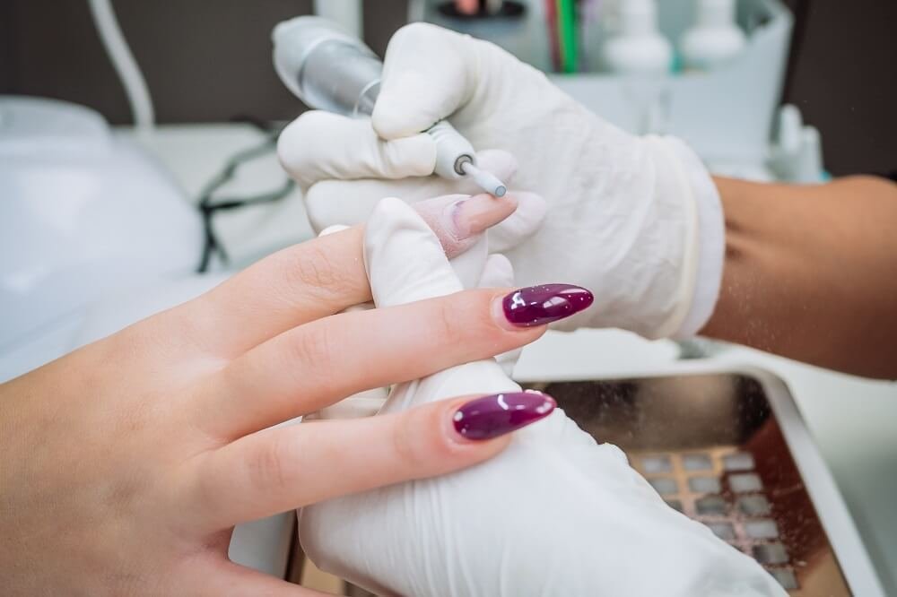 professional-esthetician-using-electric-nail-file-drill-remove-acrylic-gel-from-nails